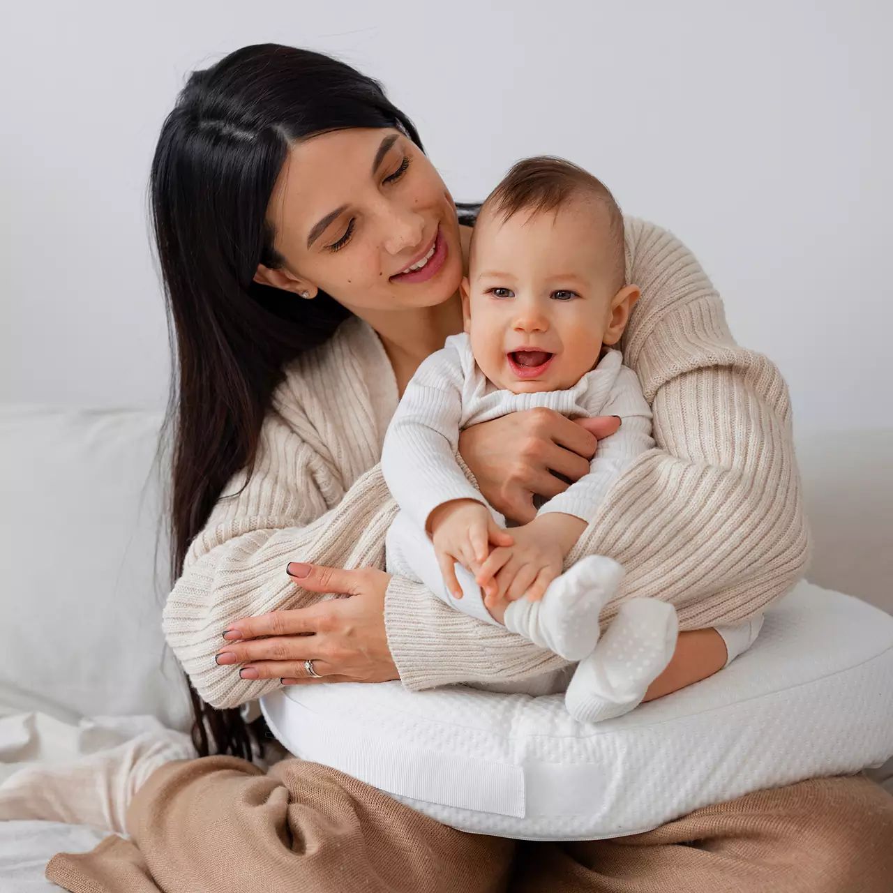 Une mère assise sur un lit, tenant dans ses bras son bébé souriant